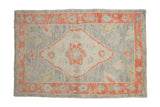 Distressed Oushak rug with a silver-blue field, central diamond medallion, and a grapefruit-red floral border.