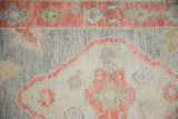 Textured close-up of an Oushak rug's hand-knotted pile in ivory, silver, and grapefruit red.