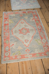 Two small distressed Oushak rugs with soft silver and red-orange tones on a wood floor.