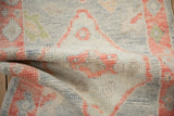 The soft, even wool pile of a distressed Oushak rug with grapefruit-red and silver-blue tones.