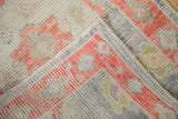Folded corner of a distressed Oushak rug showing the hand-knotted pile and intact side cord.