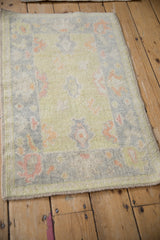 Distressed Oushak rug corner with lime green field, pink palmettes, and original side cord selvage.