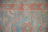Distressed Oushak rug detail showing ruby red grapefruit border and sky blue blossoms.