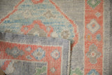 Folded edge of distressed Oushak rug, showing intact side cord and muted blue-peach pile.