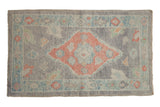 Distressed Oushak rug with pale ruby red diamond medallion and oxidized silver floral field.