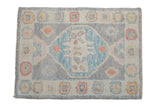 Distressed Oushak rug mat with a blue medallion and a playful pastel floral border on a silver ground.