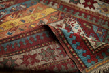 Vibrant red, teal, and gold geometric motifs on the folded antique Kazak rug.