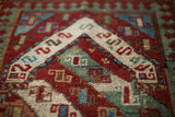 Colorful antique Kazak rug with vibrant geometric motifs in ruby red, teal, and cream.
