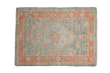Distressed Oushak rug mat in oxidized silver with a pale tangerine border and a blue central diamond medallion.