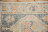 A distressed Oushak rug corner showing the even wool pile, original side cord, and floral pattern.