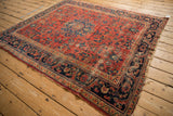Vintage Lilihan carpet corner with red floral field, navy border, and worn fringe.
