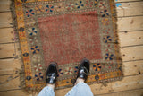 Antique Caucasian square rug with a worn dusty ruby red open field and geometric pinwheel border.