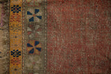 Antique Caucasian rug: worn dusty ruby red field, visible foundation, and geometric pinwheel border.