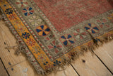 Worn corner of antique Caucasian rug, dusty red field, geometric pinwheels, frayed golden border.