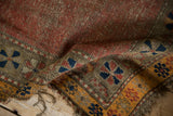 Worn dusty red field of a Caucasian rug with navy pinwheel border and tattered orange edge.