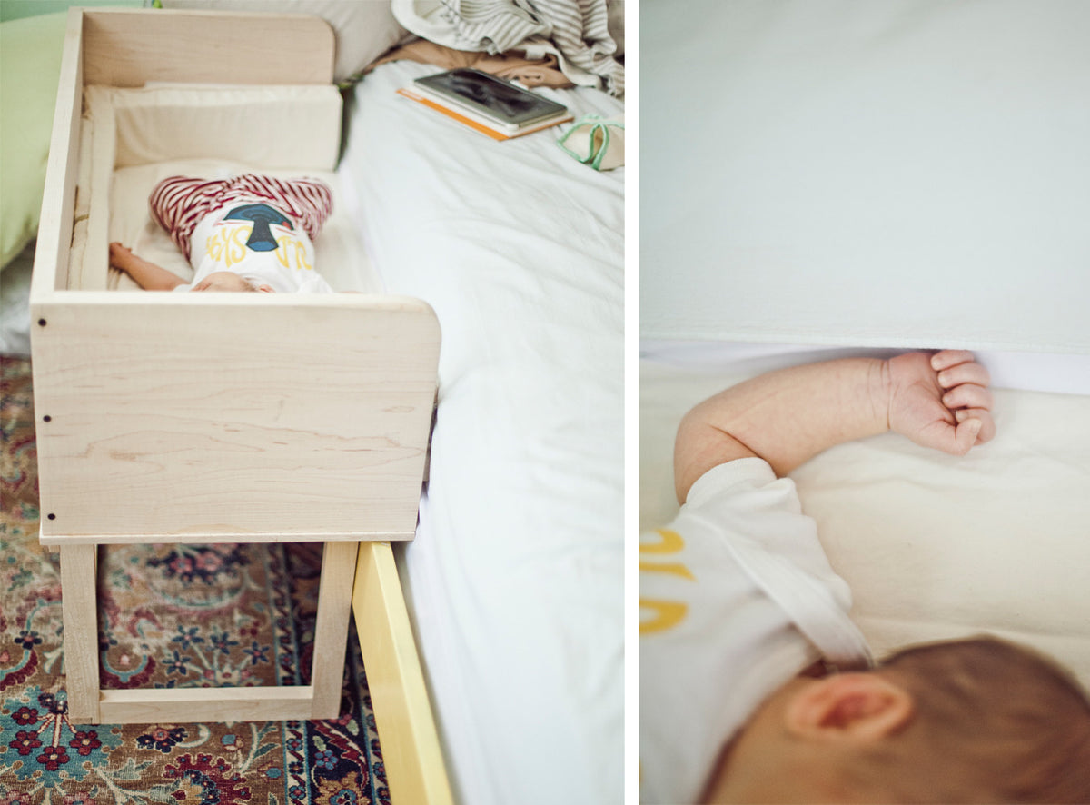 A modern white maple sidecar shown in use with a sleeping baby, placed next to a bed.