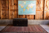 Antique primitive black wooden trunk with distressed paint, a tribal rug, and world map.