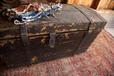 Chippy black paint and rustic iron latch on the primitive wooden trunk.