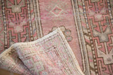 Distressed vintage Oushak rug with faded plum geometric pattern and visible foundation.