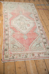 Distressed Oushak rug corner with faded raspberry border, pale green spandrel, charcoal patterns.