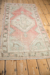 Distressed Oushak rug corner with faded raspberry and sea foam green geometric blossoms.