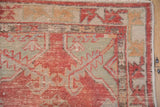 Distressed Oushak rug corner with serrated motifs in faded red and dusty green.