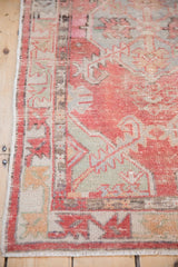Distressed vintage Oushak rug section with faded cherry red, dusty jade green, and silver geometric patterns.