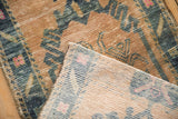 Distressed Oushak rug corner revealing worn sand, blue, pink pile and woven foundation.