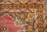 Corner of vintage Anatolian rug, faded raspberry field, gold geometric border, and stylized leaf motifs.