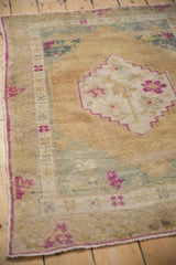 Detail of a distressed Oushak rug's corner, showing fuchsia accents against a time-softened gold and teal pile.