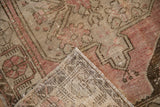 Folded corner of a vintage distressed Oushak rug showing its worn dusty rose pile and hand-knotted reverse.