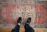 Distressed Oushak runner, central floral medallion, abrashed blush field, with feet in loafers.