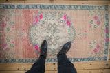 Distressed Oushak runner with pale rose abrash, roundel medallion, and vivid pink florals.