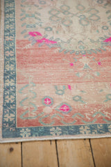 Distressed Oushak rug detail: worn pale rose field with bright pink flourishes and blue border.