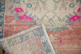 Folded distressed Oushak rug showing hand-knotted construction, abrash, and bright pink accents.