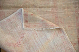 Folded corner of a distressed Oushak rug showing its hand-knotted foundation and low pile.