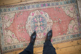 Corner view of distressed Oushak rug with faded cochineal red, blue, and pink floral motifs.