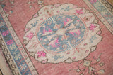 Distressed vintage Oushak rug showing cochineal red field, blue medallion, and magenta floral details.
