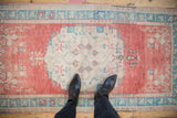 Distressed Oushak rug showing faded cherry red abrashed field and ivory roundel medallion.