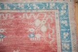 Vintage distressed Oushak rug corner with faded cherry red, ivory, and geometric dusty turquoise borders.