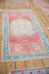 Distressed Oushak rug corner showing faded cherry red field and dusty turquoise vine-floral border.