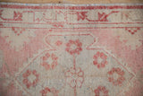 Traditional distressed Oushak rug with faded raspberry floral motifs and beige geometric border.