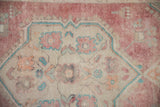 Close-up of the distressed Oushak's texture showing even wear and faded red motifs.