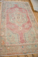 Angled view of a vintage distressed Oushak rug showing its faded red, turquoise, and ivory colors.
