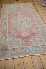 Full length angled view of a distressed Oushak rug with a faded red and turquoise medallion.