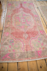 Detail of distressed Oushak runner: faded raspberry red, fuchsia, beige, and slate blue arabesques.