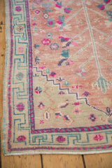 Oushak rug corner with distressed rose gold field, dusty teal key border, magenta blossoms.