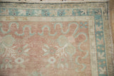 Distressed Oushak rug corner: dusty cochineal field, blue-green curvilinear motifs, patterned border.