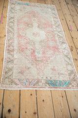 Angled view of a vintage Oushak runner showing its faded dusty rose medallion and geometric border.