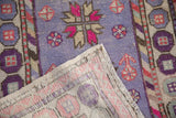 Distressed Oushak rug's folded corner reveals hand-knotted foundation, lavender, pink, and beige motifs.